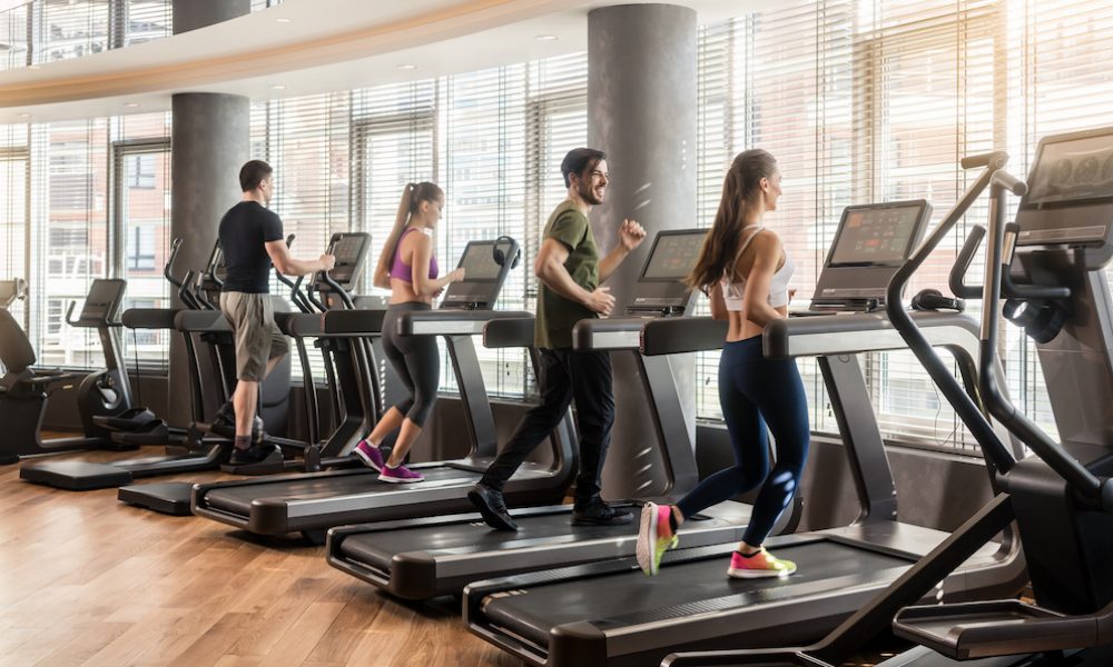 Group of four people, men and women, running on treadmills in modern and luminous fitness gym